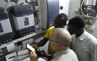 Werner, Bosuglo und Carlos im Batterieraum vom Radio Radford in Tumu schauen auf ein Handy