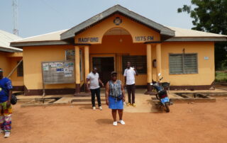Tosin, Abigail und John stehen vor dem Radford Radio in Tumu