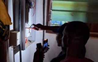 Mit einer Handylampe und unter Aufsicht seines Ausbilders Bosuglo schließt Attah am stromlosen elektrischen Schaltschrank die wichtigen Stromkreise.