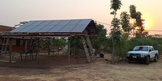 Die PV-Anlage in Bimbilla von vorne, daneben ein Pickup-Truck, ein gängiges Auto für Ghana, mit einem schönen Sonnenuntergang im Hintergrund.