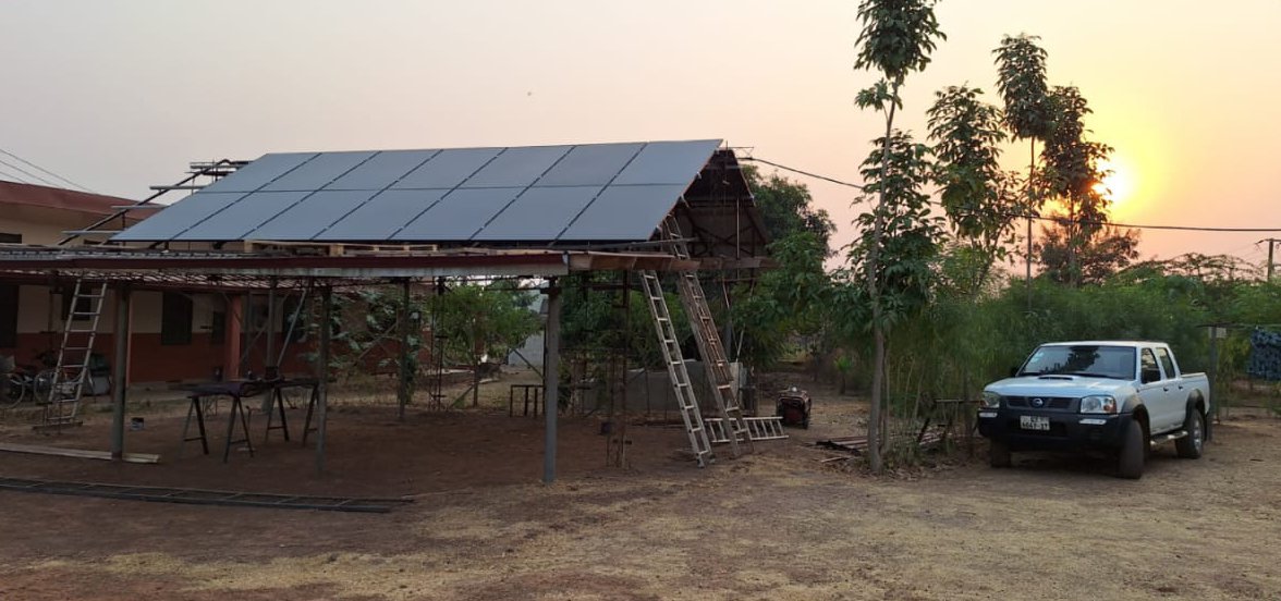 Die PV-Anlage in Bimbilla von vorne, daneben ein Pickup-Truck, ein gängiges Auto für Ghana, mit einem schönen Sonnenuntergang im Hintergrund.